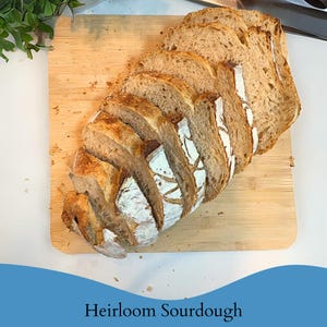 May include: Sliced loaf of heirloom sourdough bread on a wooden cutting board. The bread has a golden-brown crust and a light-colored interior. The text "Heirloom Sourdough" is at the bottom of the image.