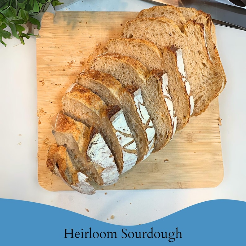 May include: Sliced loaf of heirloom sourdough bread on a wooden cutting board. The bread has a golden-brown crust and a light-colored interior. The text "Heirloom Sourdough" is at the bottom of the image.