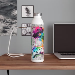 Könnte beinhalten: Eine weiße, isolierte Wasserflasche mit einem farbenfrohen Design von Videospiel-Controllern. Die Controller sind in leuchtenden Farben von Pink, Grün, Blau und Gelb dargestellt, mit einem Spritzeffekt auf grauem Hintergrund. Die Flasche ist ca. 25 cm hoch.