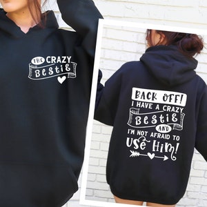 May include: Black hooded sweatshirt with white text that reads "The Crazy Bestie" on the front and "Back Off! I have a crazy Bestie and I'm not afraid to use him!" on the back.