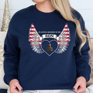 May include: Navy blue sweatshirt with a white heart and American flag wings. The heart has a photo of a person in military uniform. The text "In loving memory of my son" is above the heart.