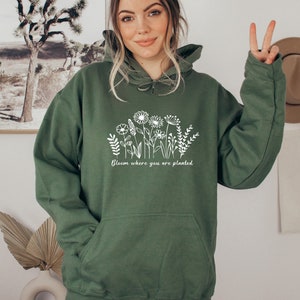 May include: A green hooded sweatshirt with a white graphic of flowers and the text "Bloom where you are planted".