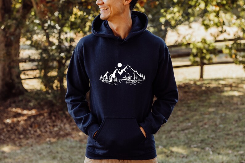 K&ouml;nnte beinhalten: Ein marineblauer Kapuzenpullover mit einem wei&szlig;en Motiv von Bergen, einem See und einem Vollmond.