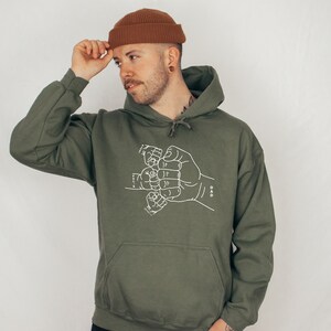 May include: A green hooded sweatshirt with a white graphic of several hands clasped together in a fist bump. The text "DAD" is printed on the right side of the graphic.