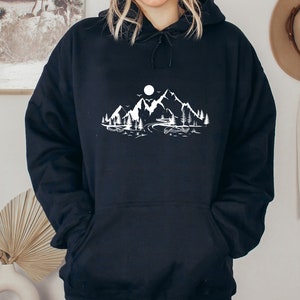 K&ouml;nnte beinhalten: Schwarzer Kapuzenpullover mit einem wei&szlig;en Motiv von Bergen, einem See und einem Mond.