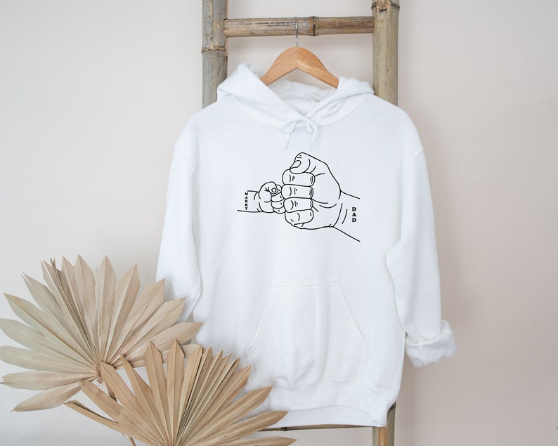 May include: White hooded sweatshirt with a black line drawing of two fists bumping, one labeled "Dad" and the other "Little."