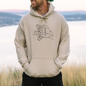 May include: A beige hoodie with a black graphic of five hands clasped together in a fist. The graphic is labeled "DAD".