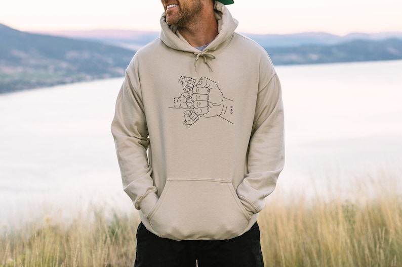 May include: A beige hoodie with a black graphic of five hands clasped together in a fist. The graphic is labeled "DAD".