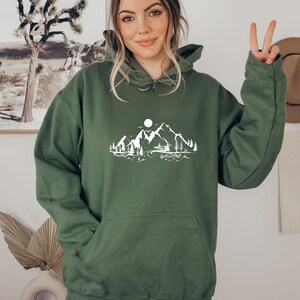 K&ouml;nnte beinhalten: Ein gr&uuml;ner Kapuzenpullover mit einem wei&szlig;en Aufdruck von Bergen, einem See und einem Mond.