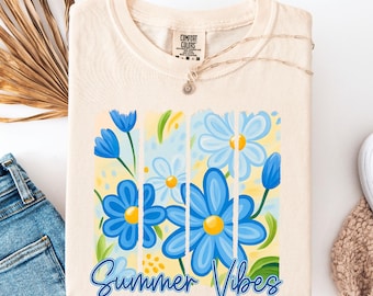 May include: Cream-colored Comfort Colors t-shirt featuring a floral design with blue flowers and the text "Summer Vibes" in a script font. The flowers have yellow centers and are set against a yellow and light blue background.