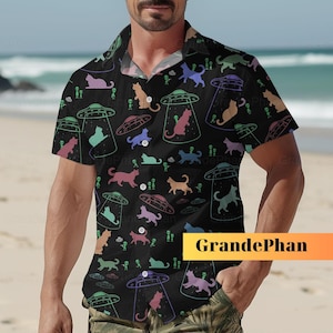 Könnte beinhalten: Ein schwarzes, kurzärmeliges Hemd mit Knöpfen und einem bunten Muster aus Katzen und fliegenden Untertassen. Das Hemd hat einen Kragen und eine Tasche auf der linken Seite. Der Text "GrandePhan" ist in der unteren rechten Ecke des Hemdes aufgedruckt.