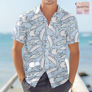 May include: A light blue short-sleeved button-down shirt with a white shark pattern. The shirt has a button-up collar and a pocket on the left side.
