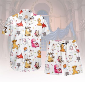 Puede incluir: Conjunto de camisa blanca de manga corta y pantalón corto a juego. El conjunto presenta un estampado repetido de gatos de dibujos animados de colores, estrellas y huellas de patas. El pantalón corto tiene un cordón negro.