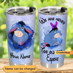 Może przedstawiać: Niebieski i biały kubek ze stali nierdzewnej z akwarelowym tłem przedstawiającym Eeyora z Kubusia Puchatka. Kubek ma czarną pokrywkę i uchwyt. Na kubku nadrukowany jest tekst "We are never too old for Eeyore". Na drugiej stronie kubka nadrukowany jest tekst "Your Name".