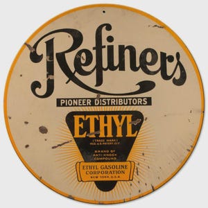 May include: Round vintage metal sign with a cream-colored background and a yellow border. The sign features the word "Refiners" in large black script, along with the text "Pioneer Distributors" and "Ethyl." The sign also includes the text "Ethyl Gasoline Corporation, New York, U.S.A."
