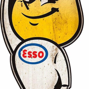 May include: A vintage-style Esso gas station sign featuring a cartoon character with a yellow head and white body. The character is wearing a blue and red oval badge with the word "Esso" printed in white.