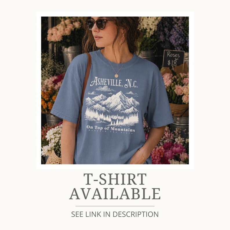 May include: A blue t-shirt featuring a mountain graphic with the text "Asheville, N.C." and "On Top of Mountains". The shirt is being worn by a person in front of a flower shop. The text "T-SHIRT AVAILABLE" is also visible.