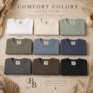 K&ouml;nnte beinhalten: Eine Comfort Colors Farbkarte mit neun gefalteten T-Shirts mit Rundhalsausschnitt in Wei&szlig;, Elfenbein, Bay, Moos, Blue Jean, Midnight, Pepper, Espresso und Schwarz. Jedes T-Shirt hat ein sichtbares Innenetikett mit dem Markennamen Comfort Colors.