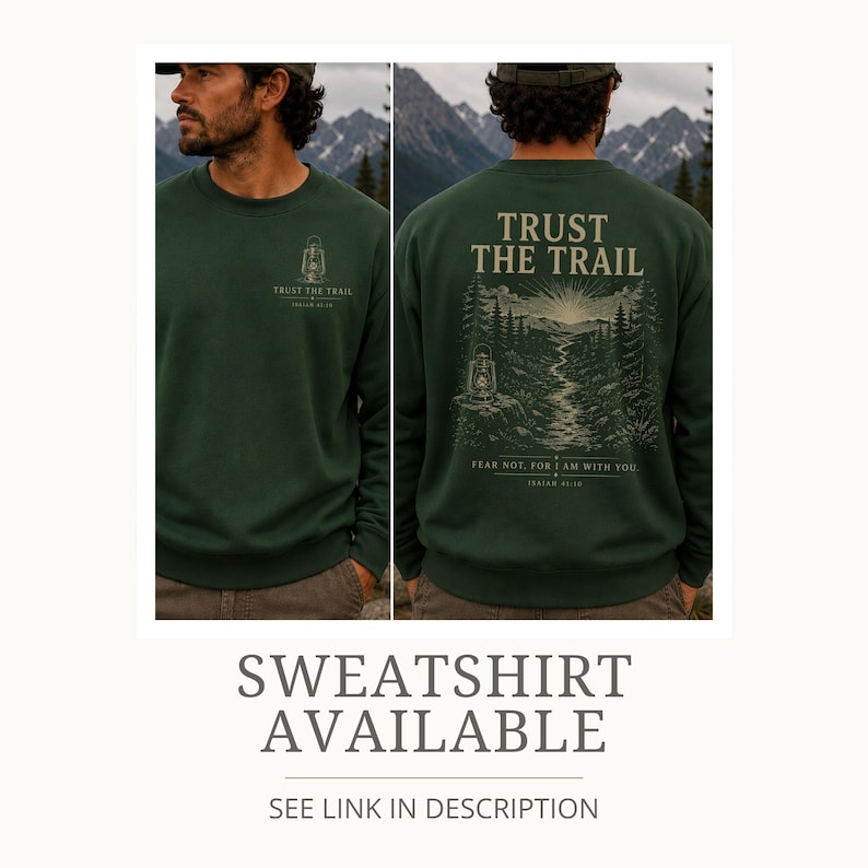 May include: A dark green crewneck sweatshirt featuring a small lantern graphic and the text "TRUST THE TRAIL" on the front left chest. The back displays a large illustration of a mountain landscape, a winding path, and a lantern with the text "TRUST THE TRAIL" and "FEAR NOT, FOR I AM WITH YOU. ISAIAH 41:10."