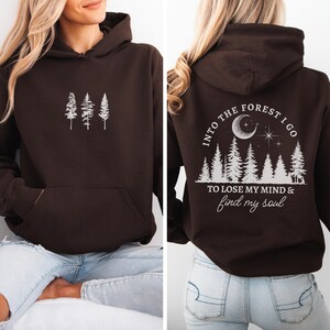 May include: Brown hooded sweatshirt with a white graphic of trees on the front and a white graphic of trees, a crescent moon, and stars with the text "Into the forest I go to lose my mind & find my soul" on the back.