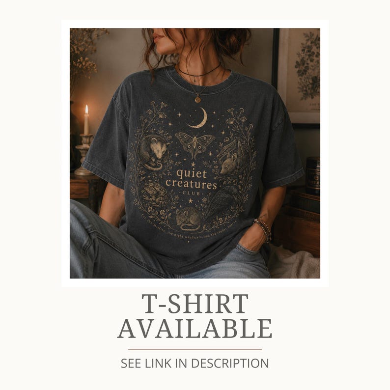 K&ouml;nnte beinhalten: Dunkelgraues T-Shirt mit einem kreisf&ouml;rmigen Design, das einen Mond, Sterne, eine Motte und verschiedene kleine Tiere zeigt. Der Text "quiet creatures club" ist zentriert. Darunter steht "T-SHIRT AVAILABLE".