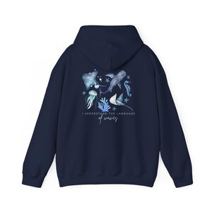 Pu&ograve; includere: Felpa con cappuccio blu navy con un design ad acquerello di vita marina, tra cui una balena, un cavalluccio marino e una medusa. La frase "I understand the language of waves" &egrave; stampata sotto. La felpa &egrave; realizzata in materiale morbido.