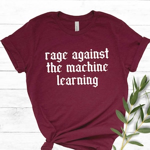 Op de afbeelding: Een maroon t-shirt met witte tekst die "rage against the machine learning" luidt.