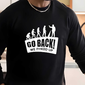 May include: Black long-sleeve sweatshirt with a white graphic of a stick figure pointing at a line of stick figures representing human evolution. The graphic says "Go Back! We F*cked Up."