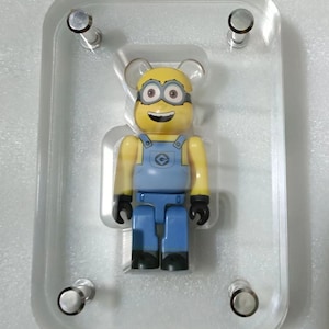 May include: A yellow and blue Minion character toy in a clear acrylic display case with four silver screws.