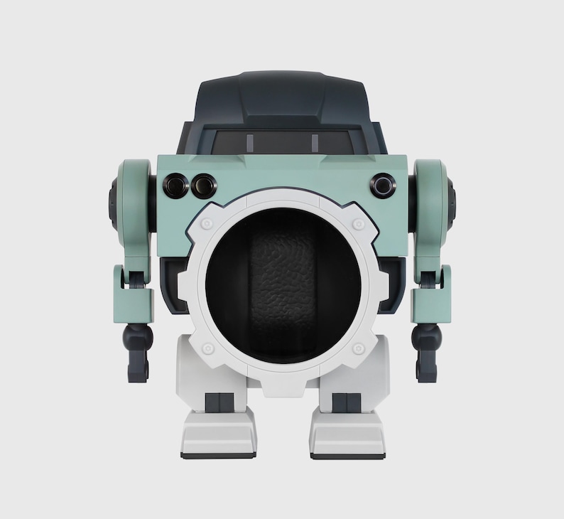 May include: A robot-like watch display case in shades of teal, gray, and white. The case has a large circular opening in the center, with articulated arms and legs. The top section is a darker gray, resembling a cockpit.