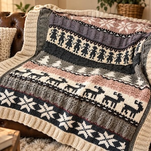 May include: A knitted throw blanket featuring a multi-coloured fair isle pattern with horizontal bands of cream, charcoal grey, and dusty rose. The design includes repeating motifs of snowflakes, stylised reindeer, pine trees, and human figures.