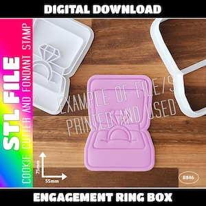 Puede incluir: Un cortador de galletas de plástico rosa en forma de caja de anillo abierta con un anillo dentro. El cortador tiene 7,5 cm de ancho y 5,5 cm de alto. El texto "EXAMPLE OF FILE/S PRINTED AND USED" es visible en el fondo.