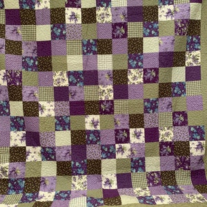 May include: A patchwork quilt with a green border and squares of various purple floral patterns, brown, and white gingham.