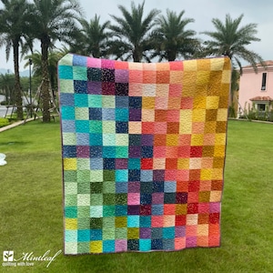 May include: A colourful patchwork quilt with a grid pattern of squares in various shades of blue, green, yellow, orange, red, and purple. The quilt is made with a variety of fabrics and has a subtle sparkle throughout.