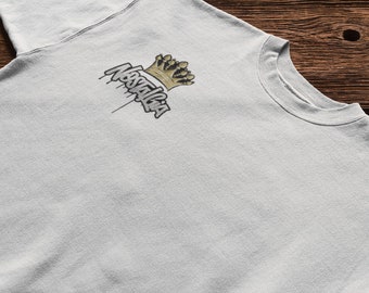 Könnte beinhalten: Ein hellgraues T-Shirt mit einer schwarzen und goldenen Grafik einer Krone und dem Wort "Nostalgia", das von der Krone tropft.
