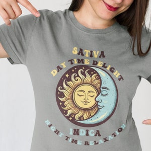 May include: Gray t-shirt with a graphic of a sun and moon. The sun has a face and says "Sativa Day Time Delight". The moon has a face and says "Indica Night Time Relaxation".