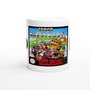 May include: White ceramic mug featuring the Super Mario Kart video game cover art. The design includes Mario, Luigi, and other characters racing on a track. The mug also has the Super Nintendo Entertainment System logo.