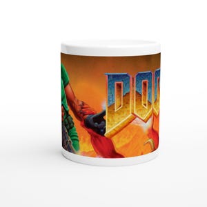 Peut inclure: Mug en céramique blanche avec le mot "DOOM" en lettres dorées et bleues. Le mug présente un fond enflammé et un personnage vêtu de vert et de noir.