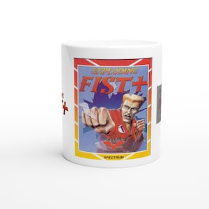 Könnte beinhalten: Weißer Keramikbecher mit einem Retro-Videospiel-Grafikdesign. Das Design zeigt den Text "EXPLODING FIST+" mit einer Figur in roter Uniform. Der Becher hat ein gelbes, rotes und blaues Farbschema, wobei auch die Wörter "FIREBIRD" und "SPECTRUM" zu sehen sind.