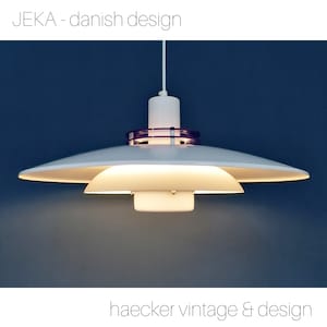 May include: A white pendant light with a purple ring around the center. The light is hanging from a white cord against a blue background. The text "JEKA - danish design" is at the top of the image and "haecker vintage & design" is at the bottom.