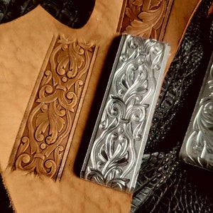 May include: Two leather tooling stamps, one silver and one brown, with a floral design. The stamps are on a brown leather surface.