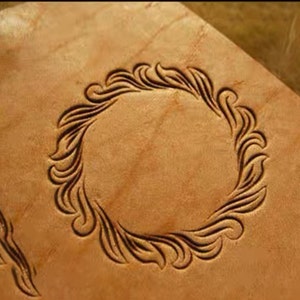 Op de afbeelding: Een close-up van een lederen handwerkproject met een decoratief, cirkelvormig, bloemmotief dat in het oppervlak is gegraveerd.