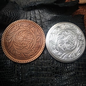May include: Two round leather tooling stamps, one brown and one silver, with a floral design. The stamps are on a black alligator-embossed surface.