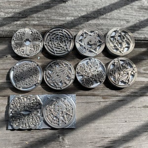 May include: Ten round metal stamp designs with intricate patterns, including a cross, a star, and a swirl. The stamps are arranged in two rows on a wooden surface.