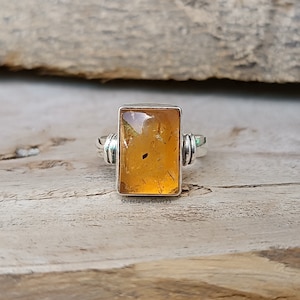 May include: A silver ring with a rectangular amber stone. The stone is a deep orange color and has a lot of inclusions. The ring is set in a simple silver band.