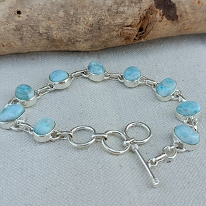 Könnte beinhalten: Ein silbernes Kettenarmband mit ovalen blauen und weißen Edelsteinperlen. Das Armband hat einen Knebelverschluss.