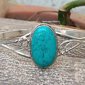 Peut inclure: Un bracelet en argent avec un ovale en turquoise serti dans une bélière en argent. Le bracelet a un design délicat et orné.