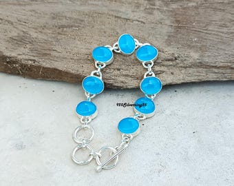 May include: A silver bracelet with oval, light blue gemstones. The gemstones are set in individual silver bezels and connected by silver links. The bracelet has a toggle clasp. The text "925 Silverking25" is visible.