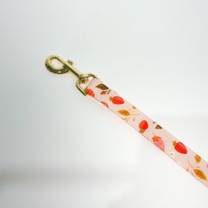 May include: A pink dog lead with a gold metal clasp and a strawberry print.