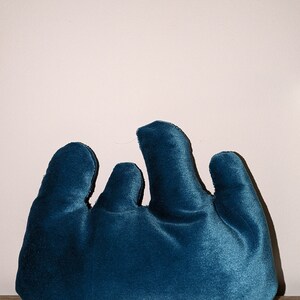 May include: A teal blue velvet pillow shaped like a hand with four fingers.